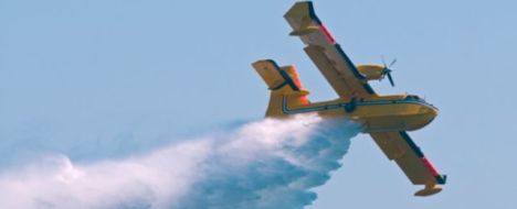 Samolot strażacki spuszcza wodę na płonący las